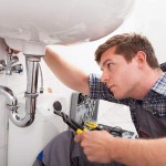 Young plumber fixing a sink in bathroom