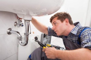 Young plumber fixing a sink in bathroom