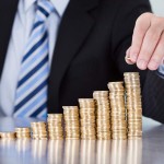 Close-up Of Businessman Hand Put Coins To Stack Of Coins